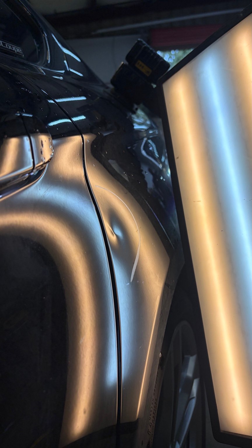 Fender panel before paintless dent repair, photographed with a repair light